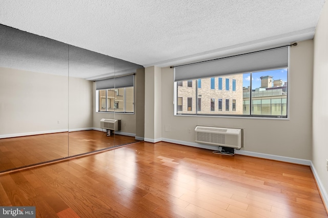 spare room with baseboards, a wall mounted AC, a textured ceiling, and wood finished floors