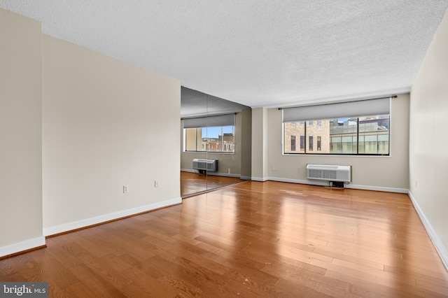 unfurnished living room featuring a wall mounted air conditioner, a textured ceiling, baseboards, and wood finished floors