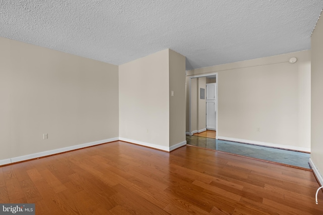 unfurnished room featuring a textured ceiling, baseboards, and wood finished floors