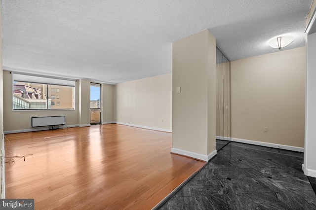 unfurnished living room featuring baseboards, a textured ceiling, and wood finished floors