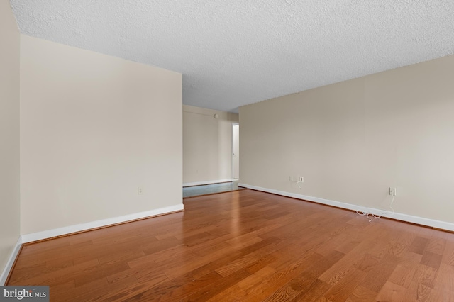 spare room featuring a textured ceiling, wood finished floors, and baseboards