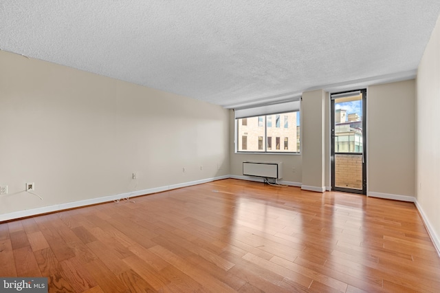 spare room featuring light wood-style floors, a textured ceiling, and baseboards