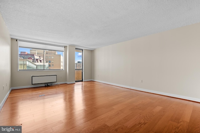 spare room featuring light wood-type flooring, a textured ceiling, and baseboards