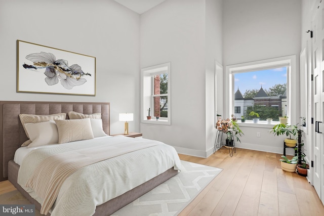 bedroom with a towering ceiling, light wood-style flooring, and baseboards