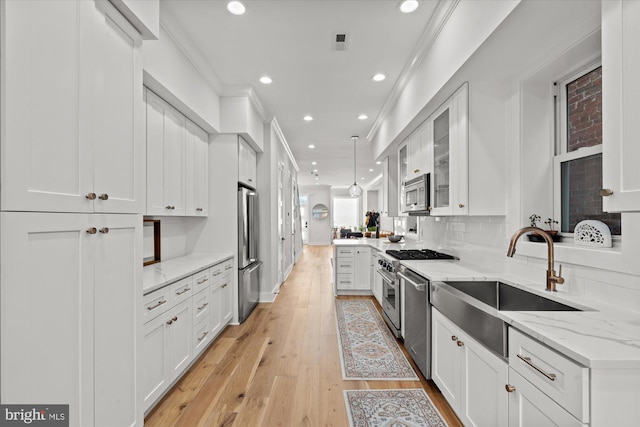 kitchen with appliances with stainless steel finishes, light wood-style floors, ornamental molding, white cabinets, and a sink