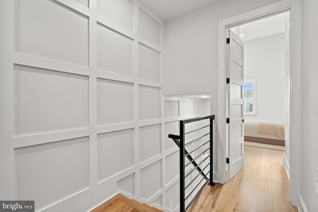 hallway with light wood finished floors, an upstairs landing, and a decorative wall