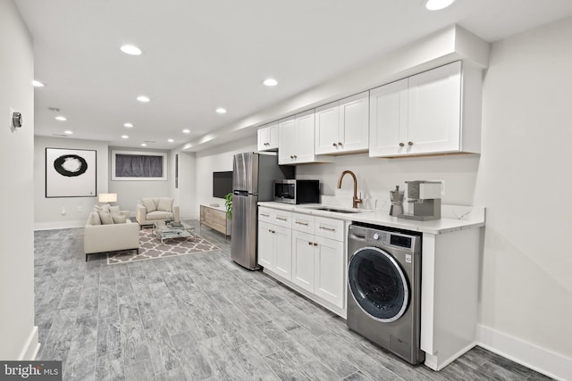 kitchen featuring a sink, white cabinets, appliances with stainless steel finishes, light wood-type flooring, and washer / dryer