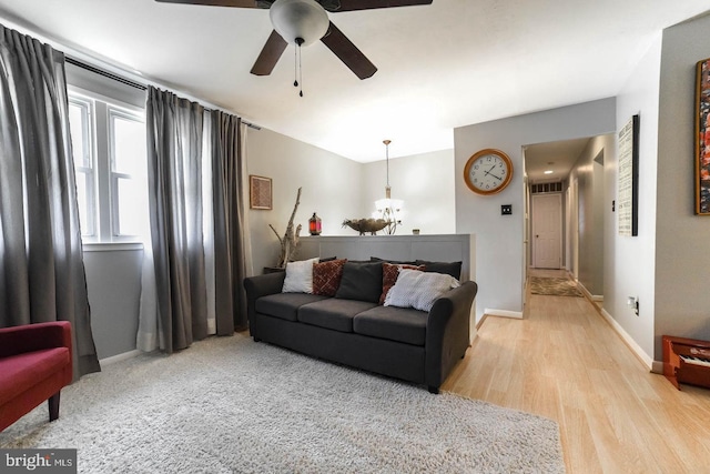 living room featuring light wood-style flooring, baseboards, and ceiling fan with notable chandelier