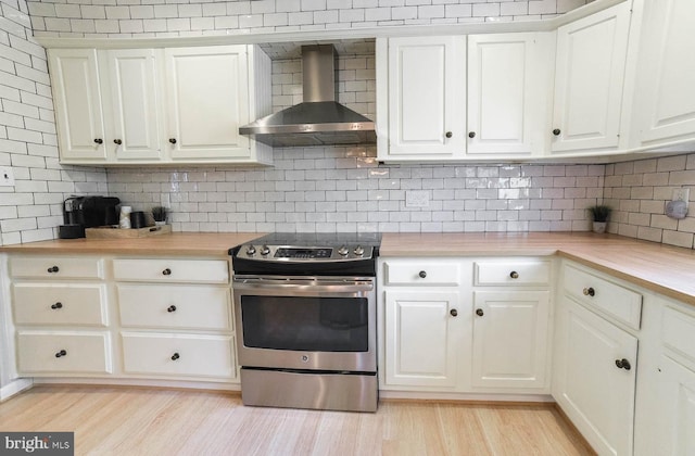 kitchen featuring light wood-style flooring, electric range, white cabinets, wall chimney range hood, and backsplash