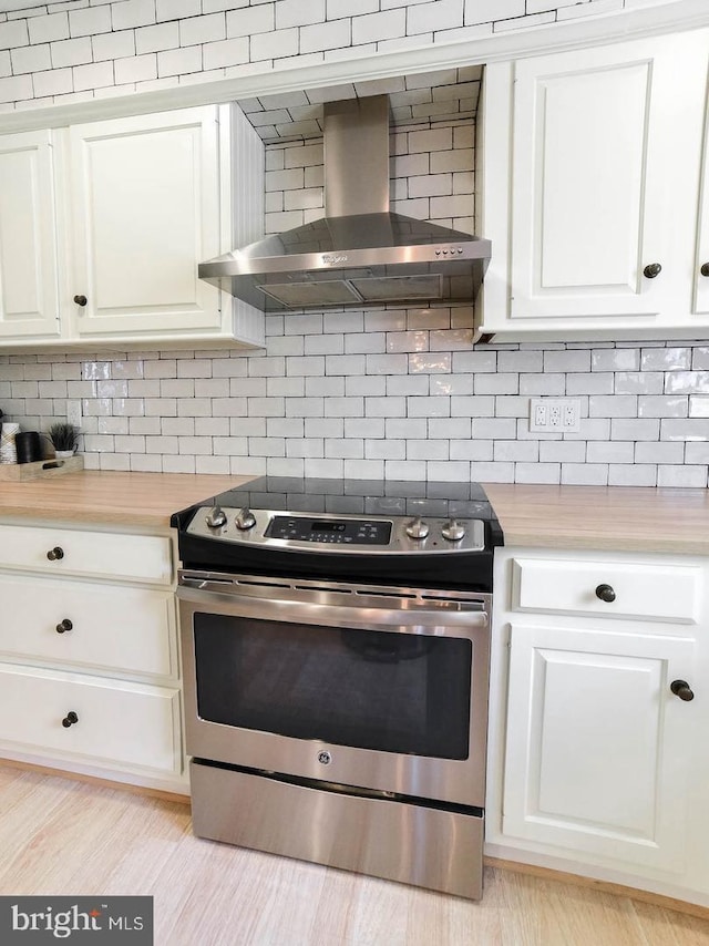 kitchen with decorative backsplash, wall chimney exhaust hood, light countertops, stainless steel range with electric cooktop, and white cabinetry