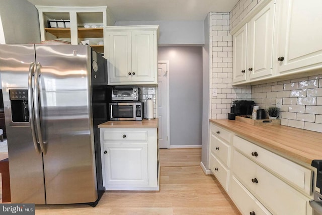 kitchen with appliances with stainless steel finishes, light wood-type flooring, white cabinets, and decorative backsplash