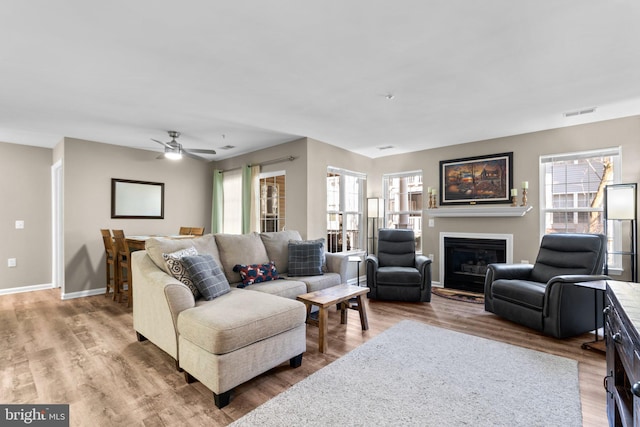 living area featuring a glass covered fireplace, visible vents, baseboards, and wood finished floors