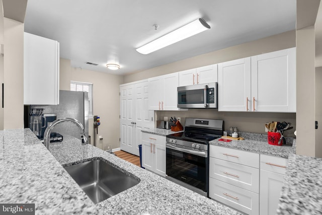 kitchen with visible vents, a sink, white cabinetry, appliances with stainless steel finishes, and light stone countertops