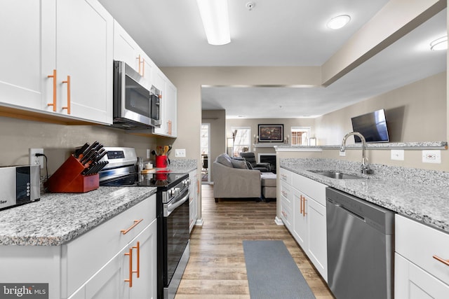 kitchen featuring a sink, light wood-style floors, appliances with stainless steel finishes, white cabinetry, and open floor plan