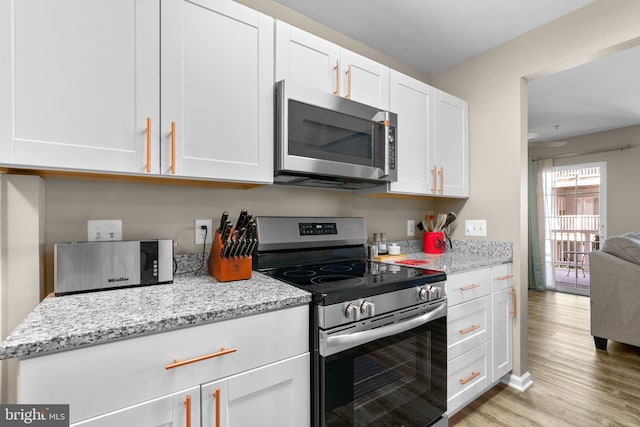 kitchen with light stone countertops, light wood-style floors, appliances with stainless steel finishes, and white cabinetry