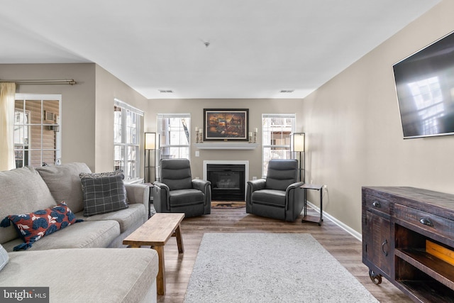 living room featuring visible vents, wood finished floors, baseboards, and a glass covered fireplace