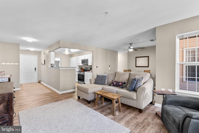 living area featuring light wood-style flooring, a ceiling fan, and baseboards