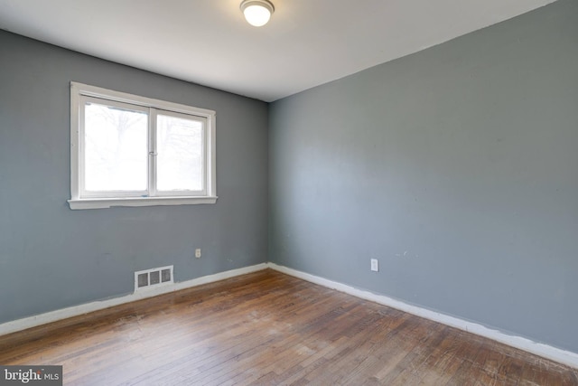 spare room with hardwood / wood-style flooring, visible vents, and baseboards