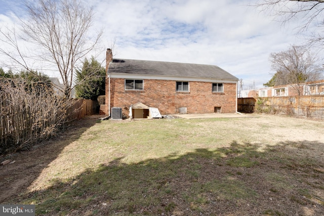 rear view of property featuring a fenced backyard, central AC, brick siding, a lawn, and a chimney