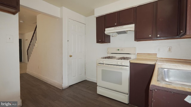 kitchen featuring light countertops, dark wood-type flooring, a sink, under cabinet range hood, and white gas range oven