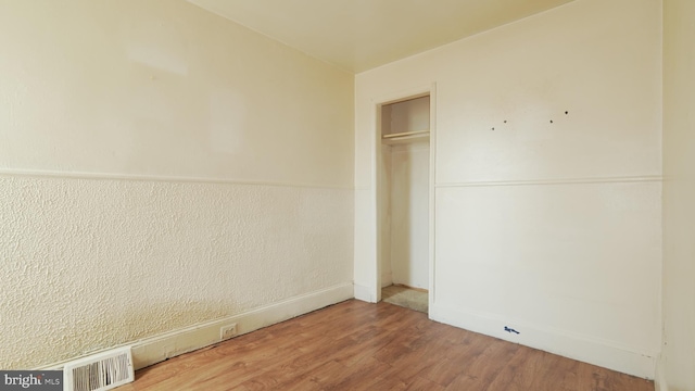 unfurnished bedroom with a wainscoted wall, a closet, wood finished floors, and visible vents