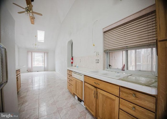 kitchen featuring tile countertops, high vaulted ceiling, a sink, a ceiling fan, and paneled dishwasher