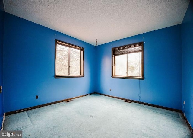 carpeted spare room featuring visible vents, a textured ceiling, and baseboards