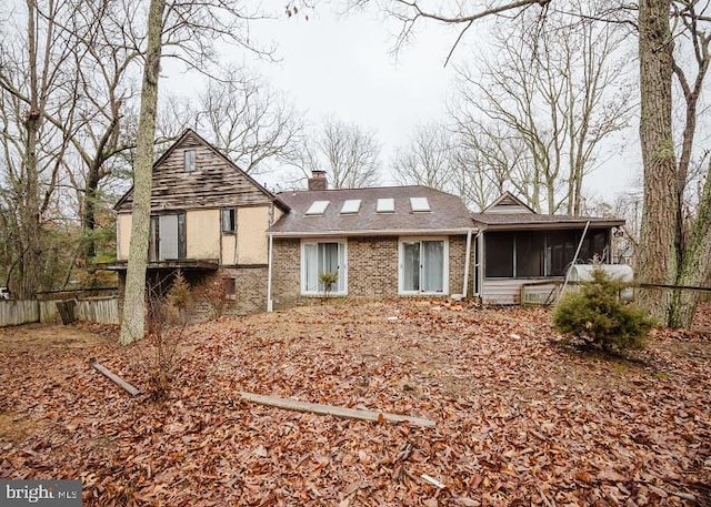 back of property featuring a sunroom, brick siding, fence, and a chimney