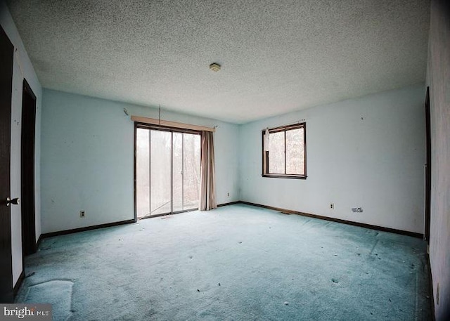 carpeted spare room featuring a textured ceiling and baseboards