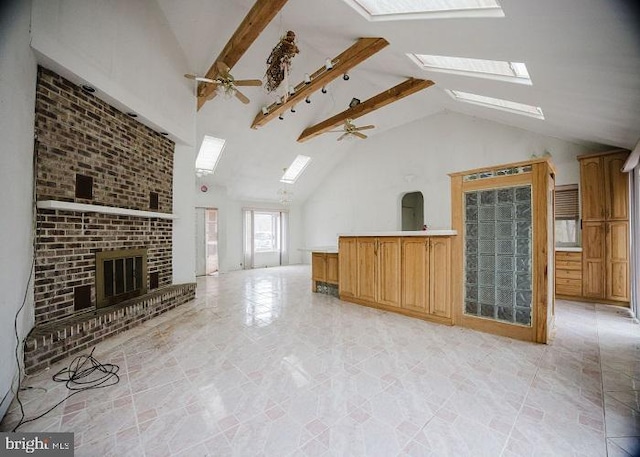 unfurnished living room with a brick fireplace, a ceiling fan, a skylight, and high vaulted ceiling