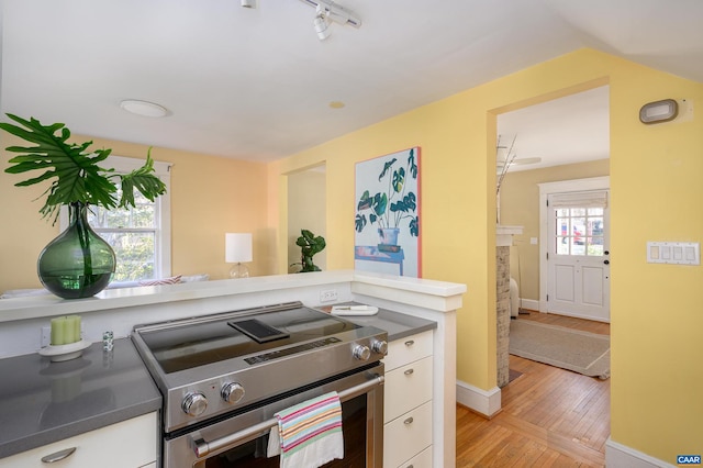 kitchen with light wood finished floors, stainless steel range with electric cooktop, white cabinetry, track lighting, and baseboards