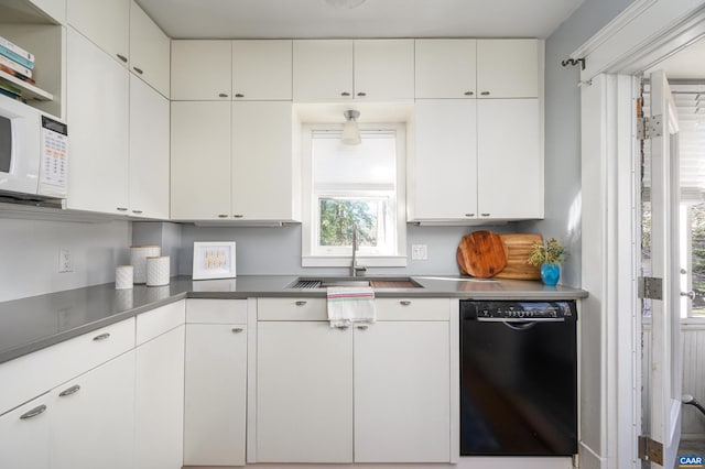 kitchen with dark countertops, white microwave, white cabinets, a sink, and dishwasher