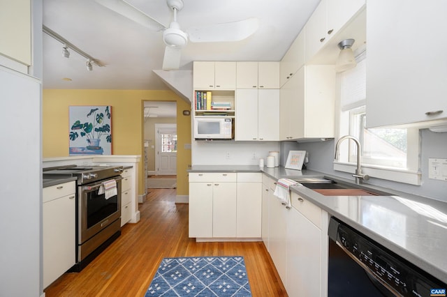 kitchen featuring black dishwasher, stainless steel electric stove, white microwave, a sink, and light wood-type flooring