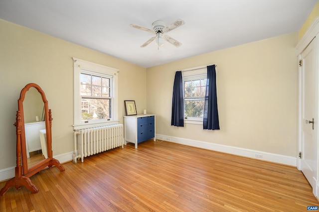 bedroom with baseboards, multiple windows, light wood-style flooring, and radiator