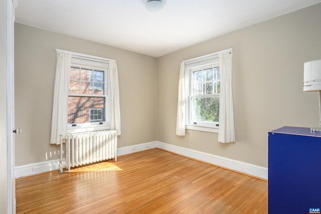 empty room with radiator, light wood-style floors, and baseboards