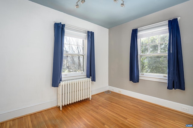 spare room featuring baseboards, radiator heating unit, and wood finished floors