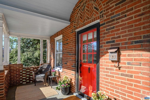 doorway to property with a porch and brick siding