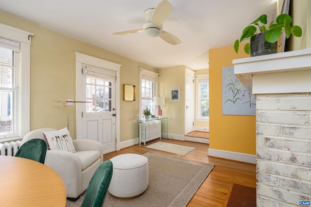 living area featuring a ceiling fan, baseboards, radiator heating unit, and wood finished floors