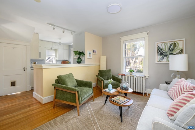 living room featuring light wood finished floors, visible vents, baseboards, radiator heating unit, and rail lighting