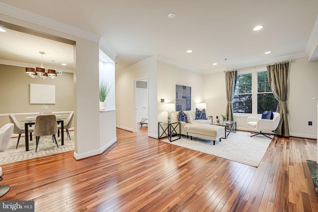 living area featuring wood-type flooring, ornamental molding, a chandelier, and baseboards