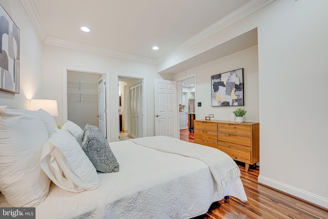 bedroom featuring baseboards, wood finished floors, a walk in closet, crown molding, and recessed lighting