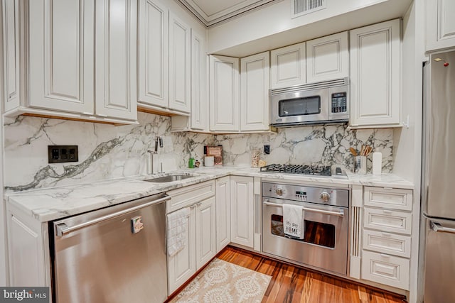 kitchen featuring light stone counters, light wood finished floors, stainless steel appliances, visible vents, and a sink