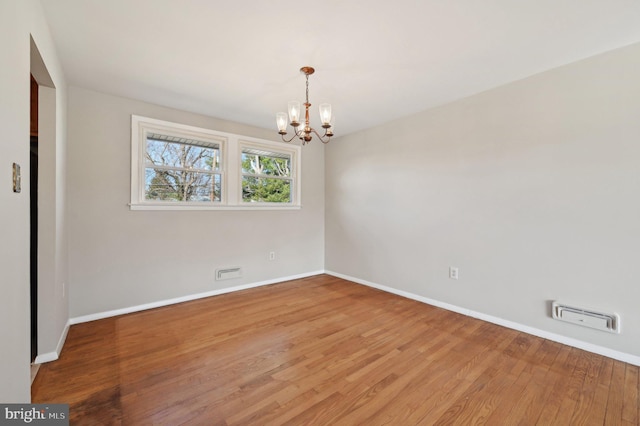 spare room featuring visible vents, baseboards, an inviting chandelier, and wood finished floors