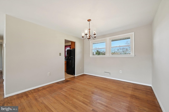 spare room with an inviting chandelier, baseboards, and light wood finished floors