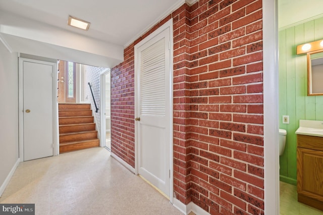 hallway featuring light floors, brick wall, and stairs