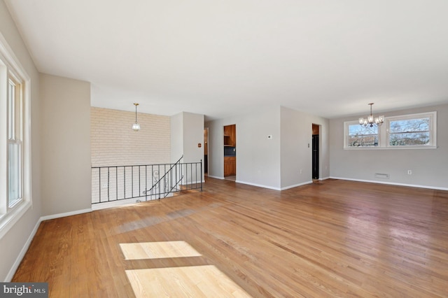 unfurnished room featuring an inviting chandelier, brick wall, baseboards, and light wood finished floors