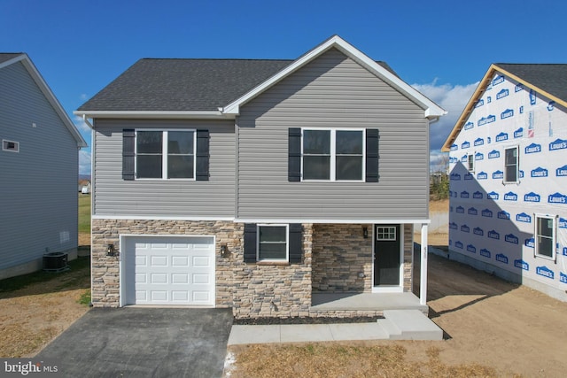 view of front of property with central air condition unit, stone siding, a garage, and aphalt driveway