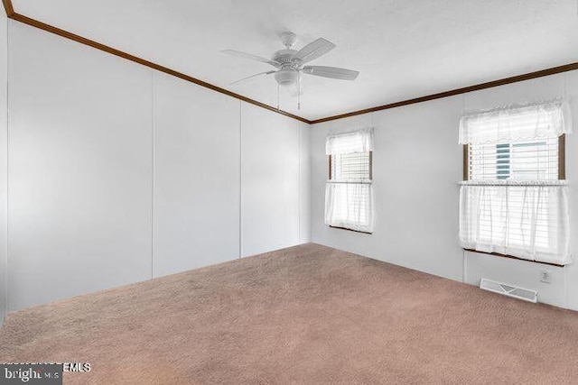 carpeted empty room with ceiling fan, a healthy amount of sunlight, visible vents, and crown molding