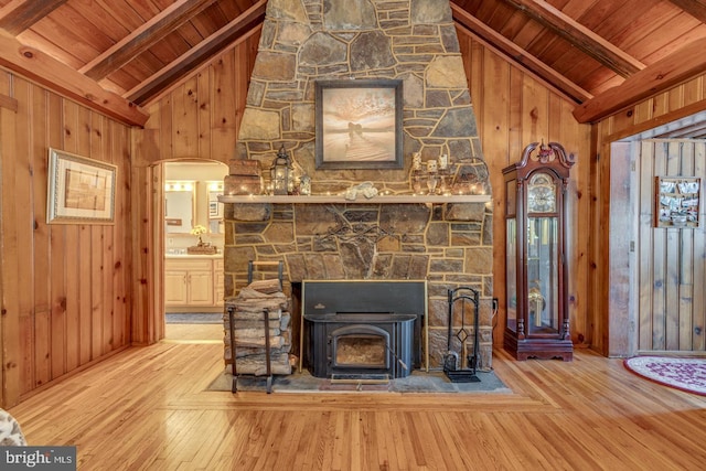 unfurnished living room featuring a wood stove, wood walls, wood-type flooring, and beamed ceiling