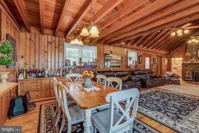 dining area featuring a fireplace, light wood finished floors, wooden walls, wooden ceiling, and ceiling fan with notable chandelier